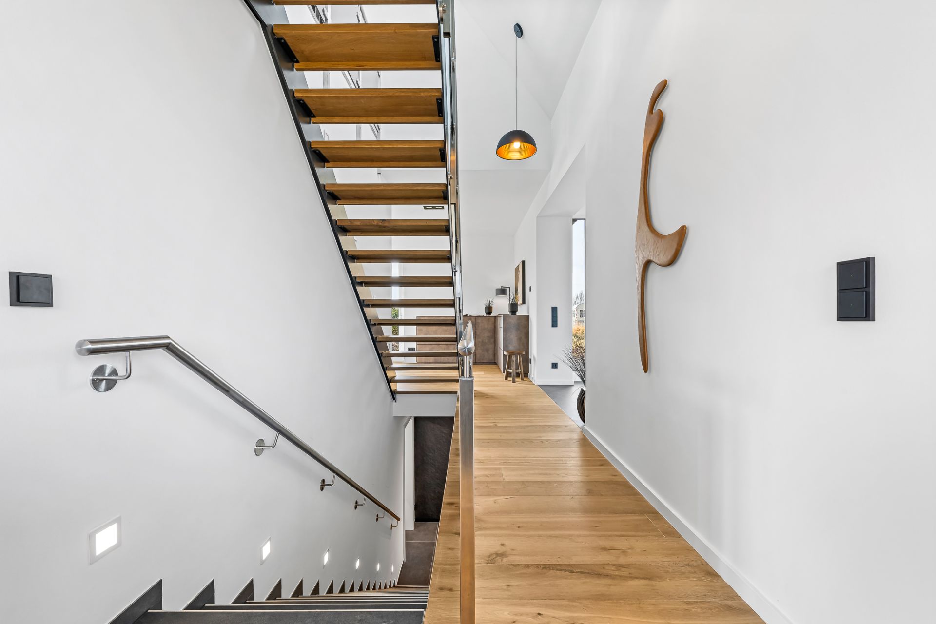 Heller Flur mit Holztreppe, Holzfußboden und moderner Wanddekoration.