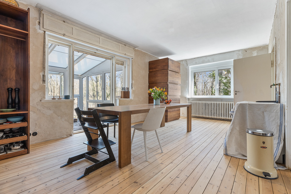Heller Raum mit Esstisch, Stühlen, Holzfußboden und großem Fenster mit Blick nach draußen.