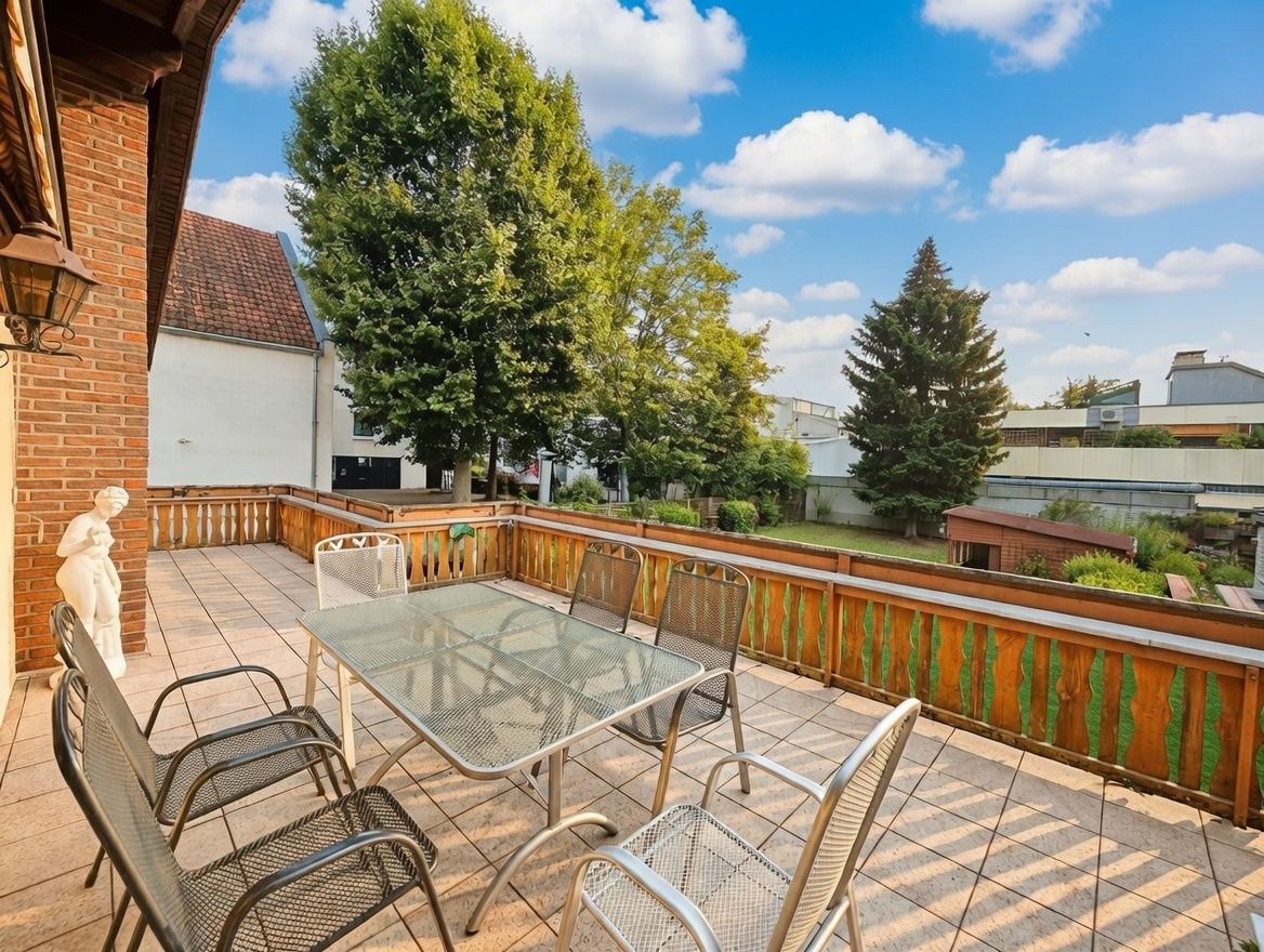 Große Terrasse mit Glastisch, sechs Stühlen und Blick auf Garten und Bäume.