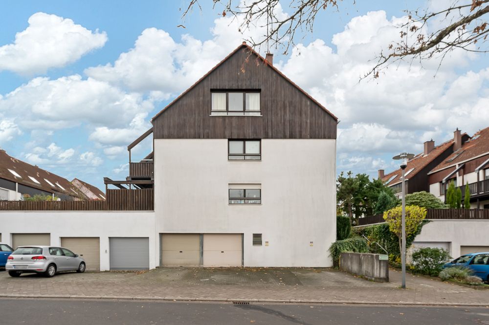 Wohnhaus mit drei Garagentoren, zwei parkenden Autos und Bäumen an der Straße.