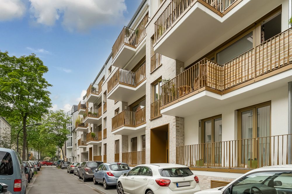Mehrstöckiges Wohnhaus mit Balkonen an einer von Autos gesäumten Straße.