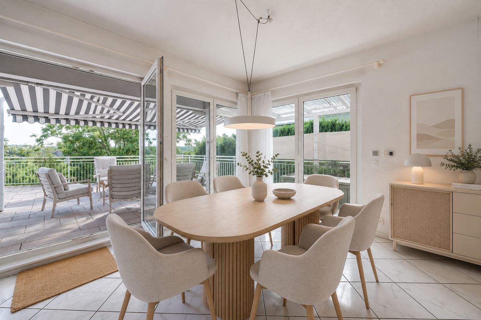 Heller Essbereich mit ovalem Holztisch, sechs Stühlen und Zugang zur Terrasse mit Markise.