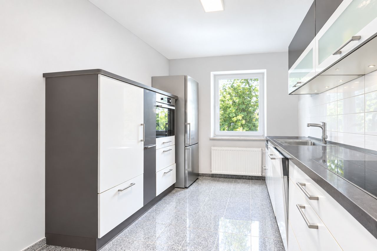 Moderne Einbauküche mit weißen Fronten, großem Fenster und Edelstahl-Kühlschrank.