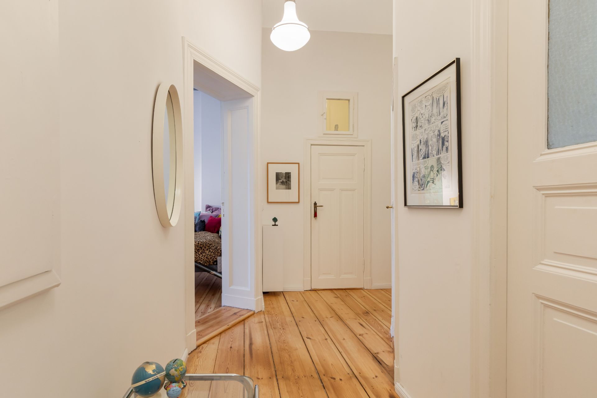Heller Flur mit Holzboden, weißen Wänden, Türen, Spiegel und gerahmtem Bild an der Wand.