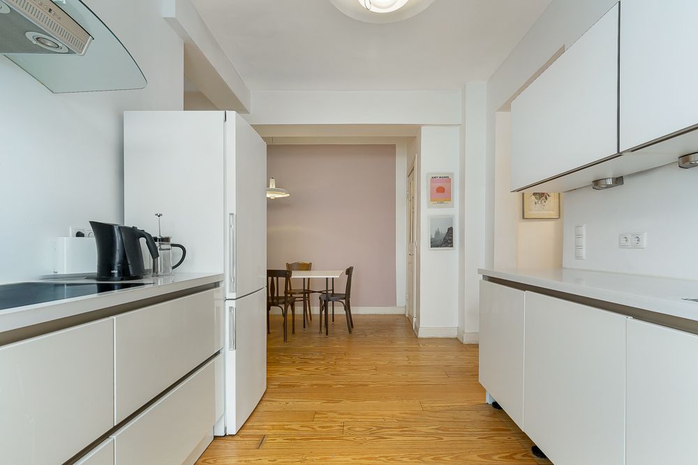Moderne weiße Küche mit Holzfußboden, Blick auf einen kleinen Essbereich mit Tisch und vier Stühlen.