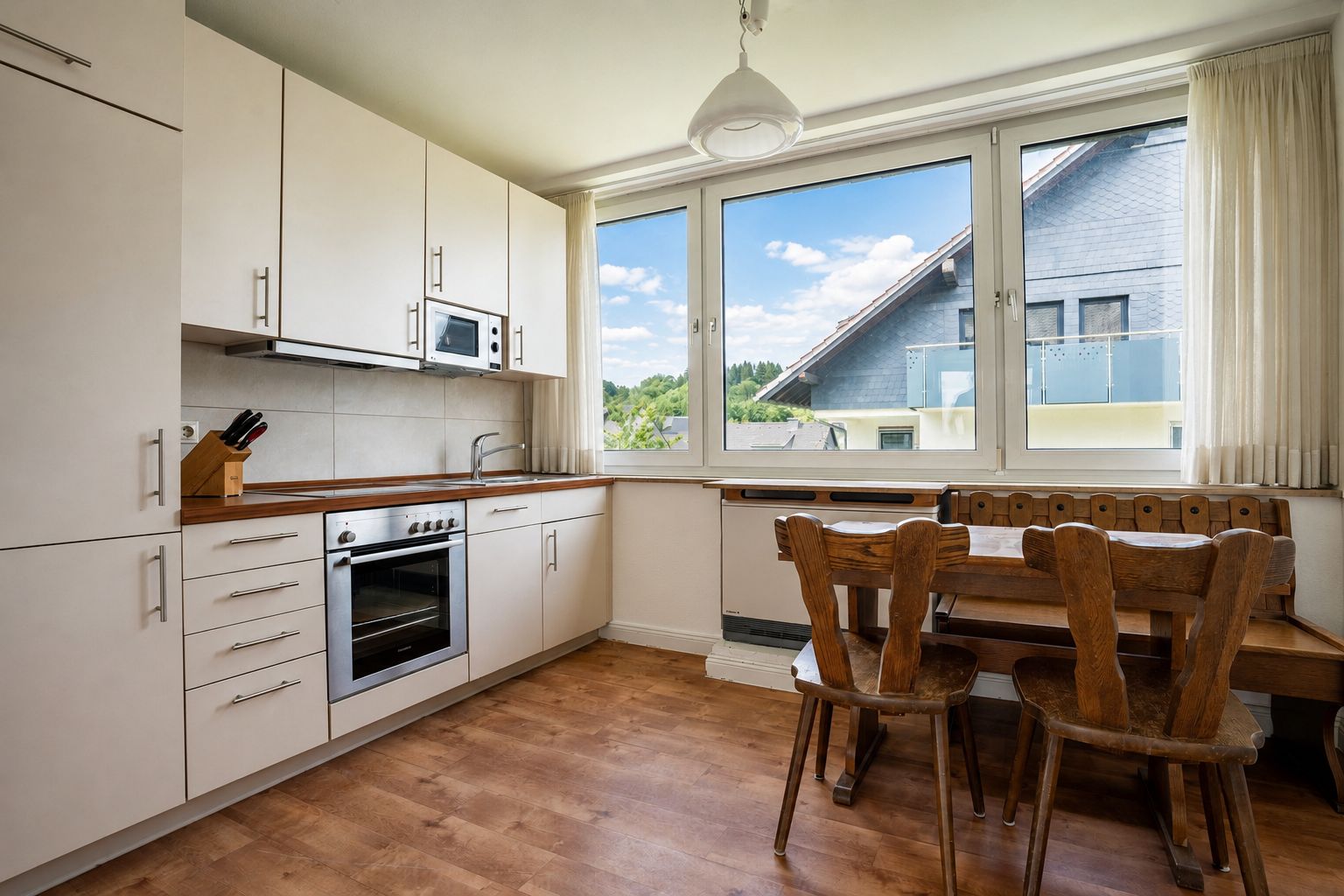 Helle Küche mit Esstisch, Holzstühlen, großem Fenster und moderner Einbauküche.