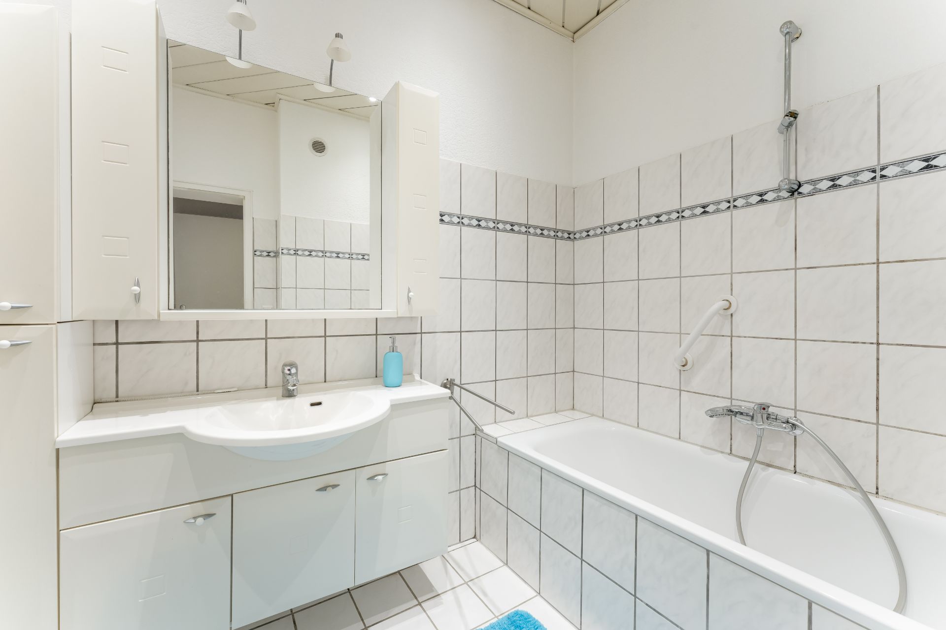 Helles Badezimmer mit Badewanne, Waschbecken, Spiegel und weißen Fliesen.