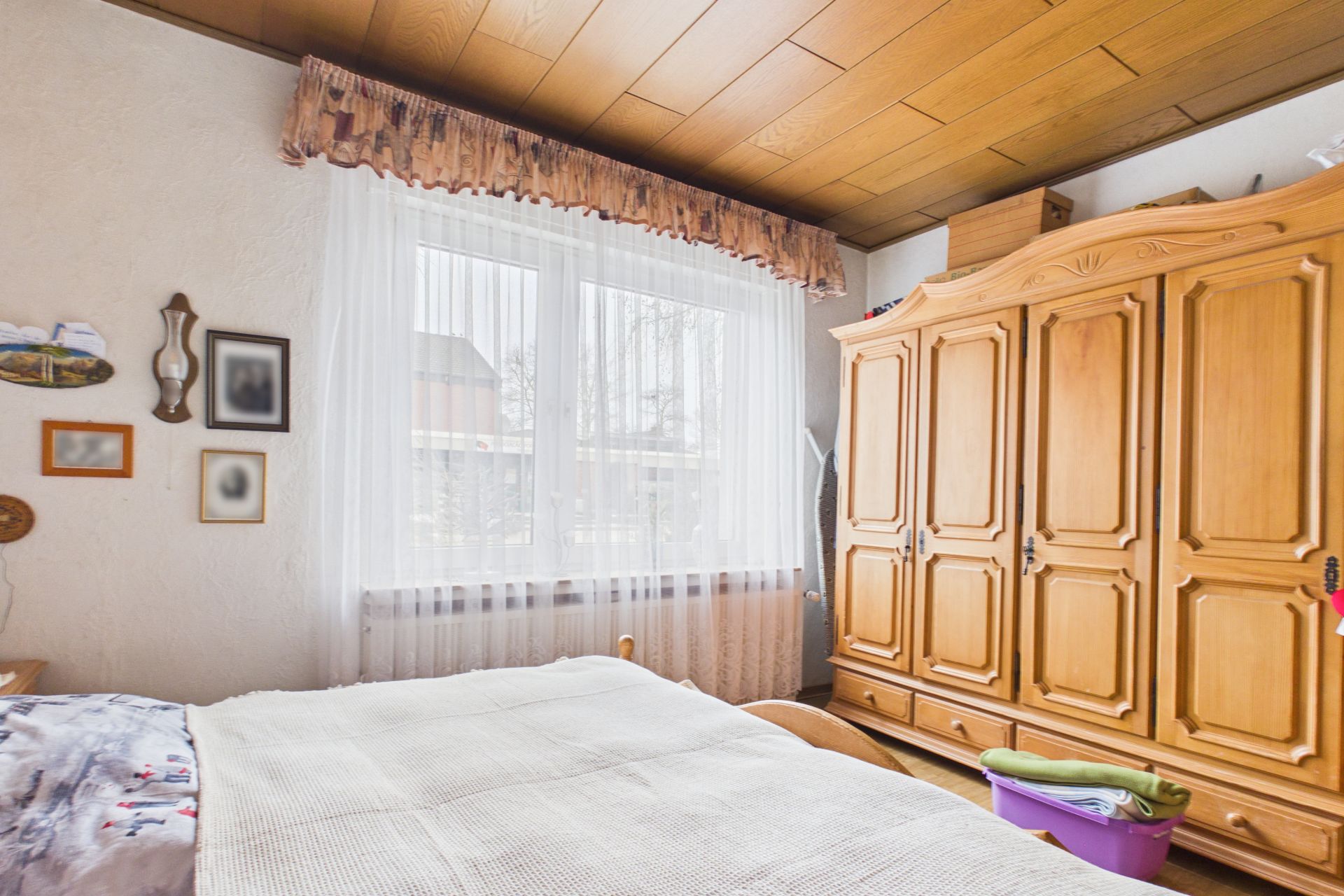 Helles Schlafzimmer mit großem Holzschrank, Bett und Fenster mit Vorhang.