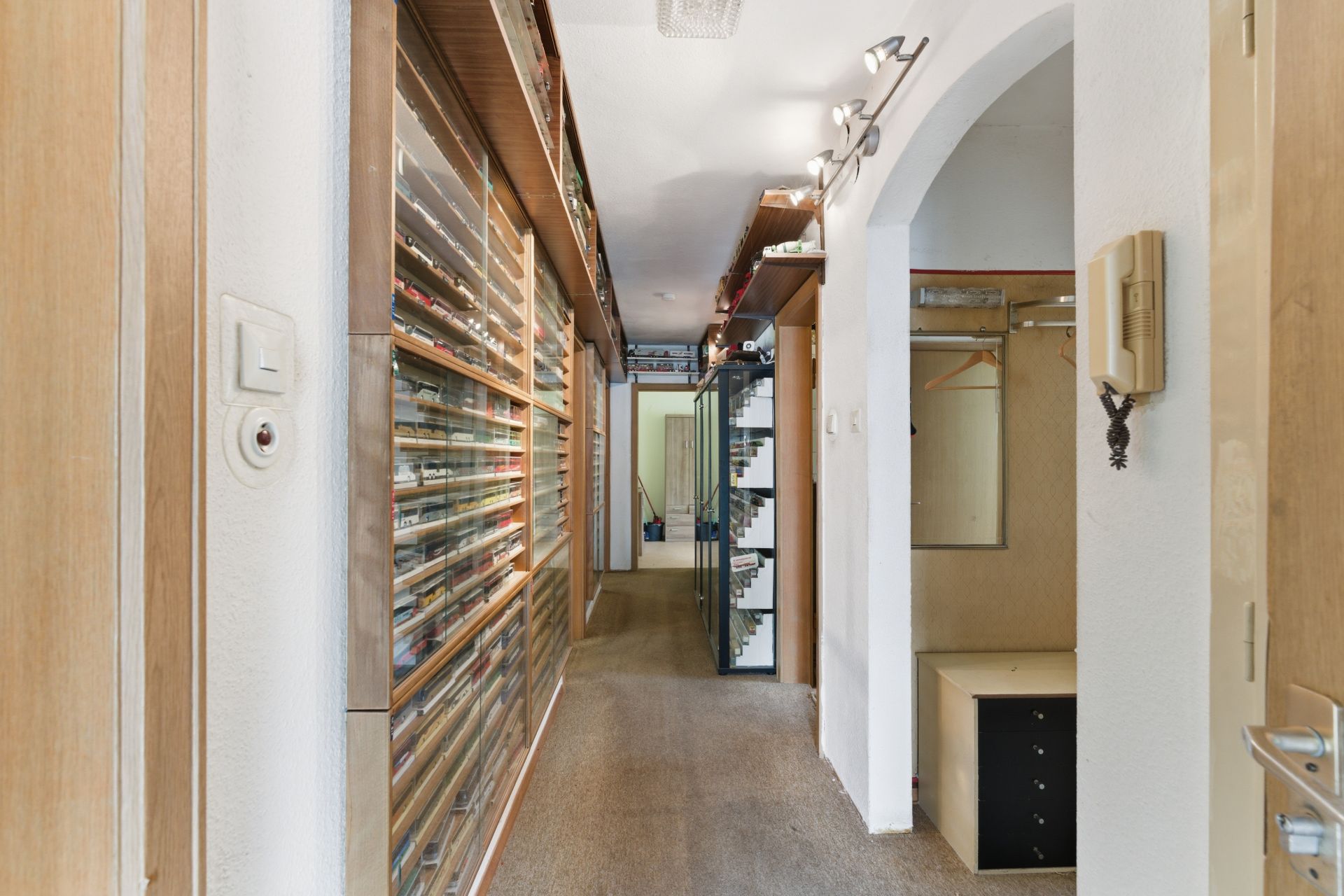 Schmaler Flur mit vielen Regalen, Spiegel und Garderobe an der Wand.