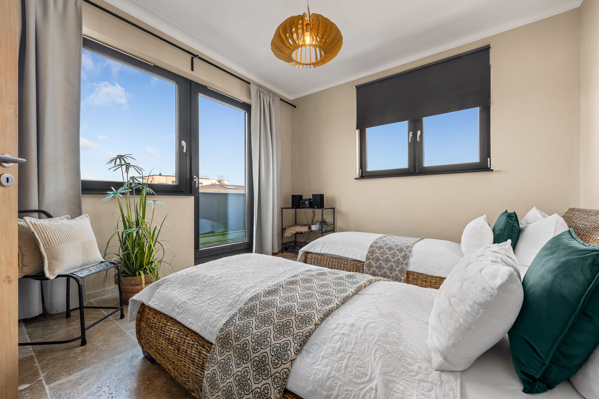 Helles Schlafzimmer mit zwei Einzelbetten, großen Fenstern und Pflanzen an der Seite.