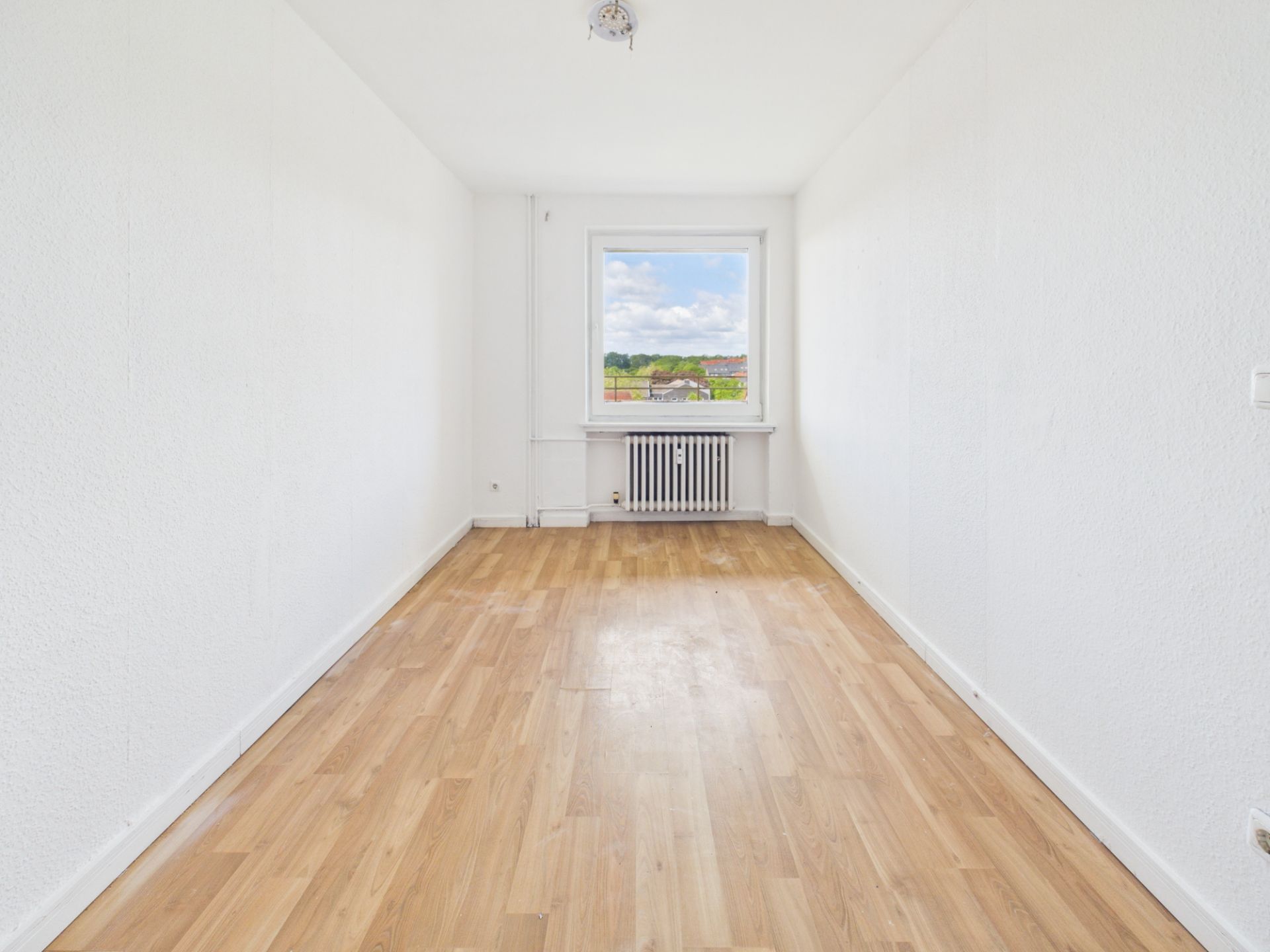 Leerer, heller Raum mit Holzfußboden, weiß gestrichenen Wänden und Fenster mit Ausblick.