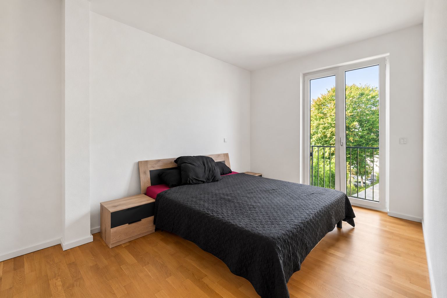 Schlafzimmer mit Doppelbett, Nachttischen und bodentiefem Fenster mit Blick ins Grüne.