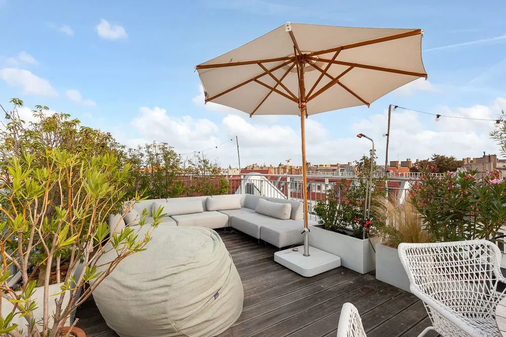 Dachterrasse mit Sitzgruppe, Sonnenschirm, Pflanzen und Sitzsack bei Tageslicht.