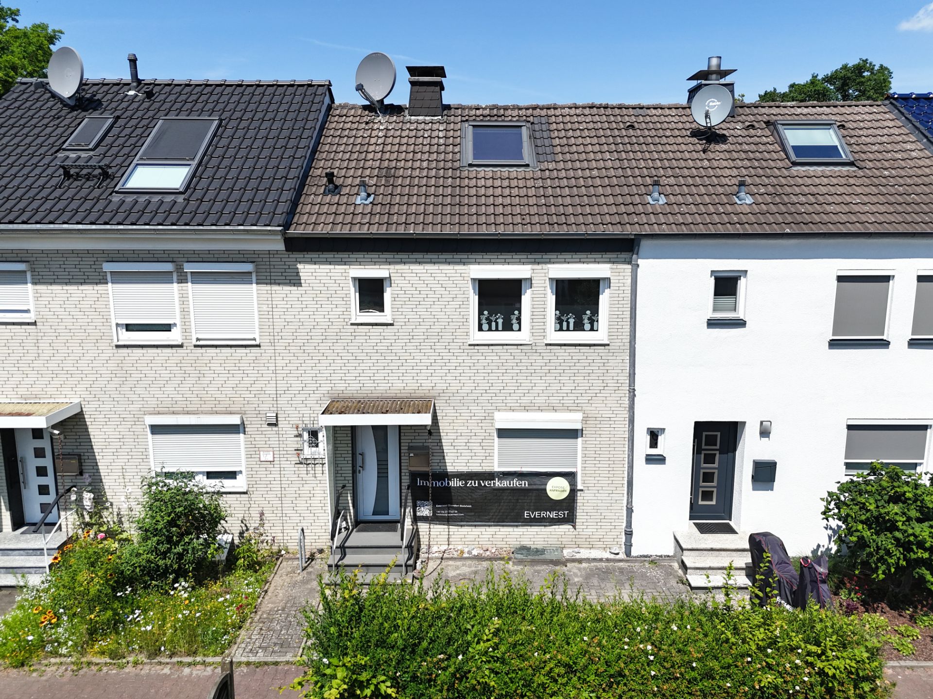 Vorderansicht eines Reihenhauses mit weißer Fassade und Vorgarten.