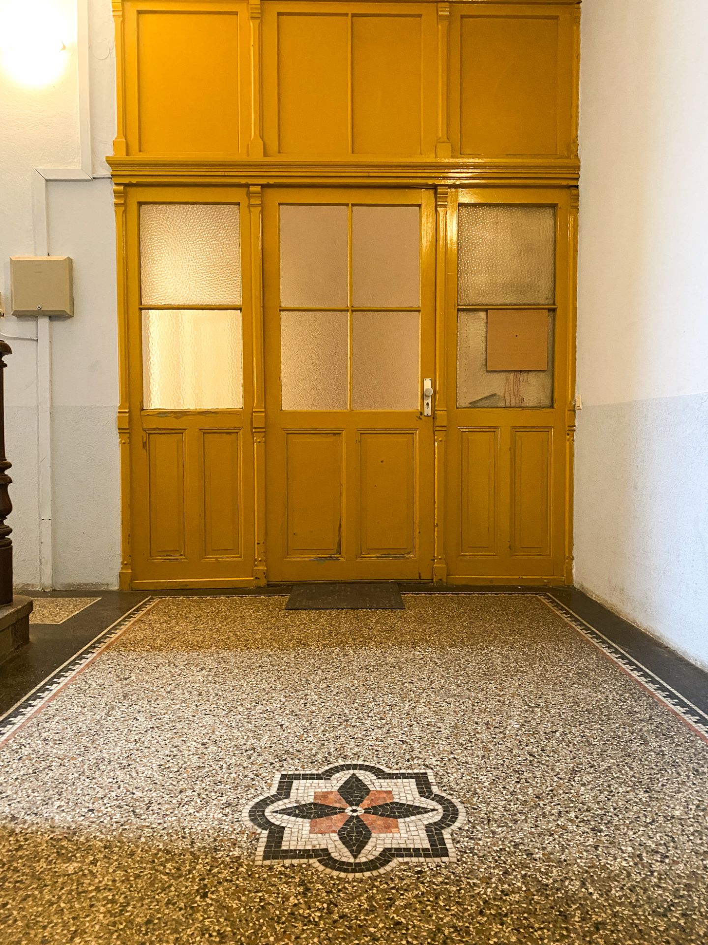 Gelbe Holztür mit Glaseinsätzen und gemustertem Mosaikboden in einem Flur.