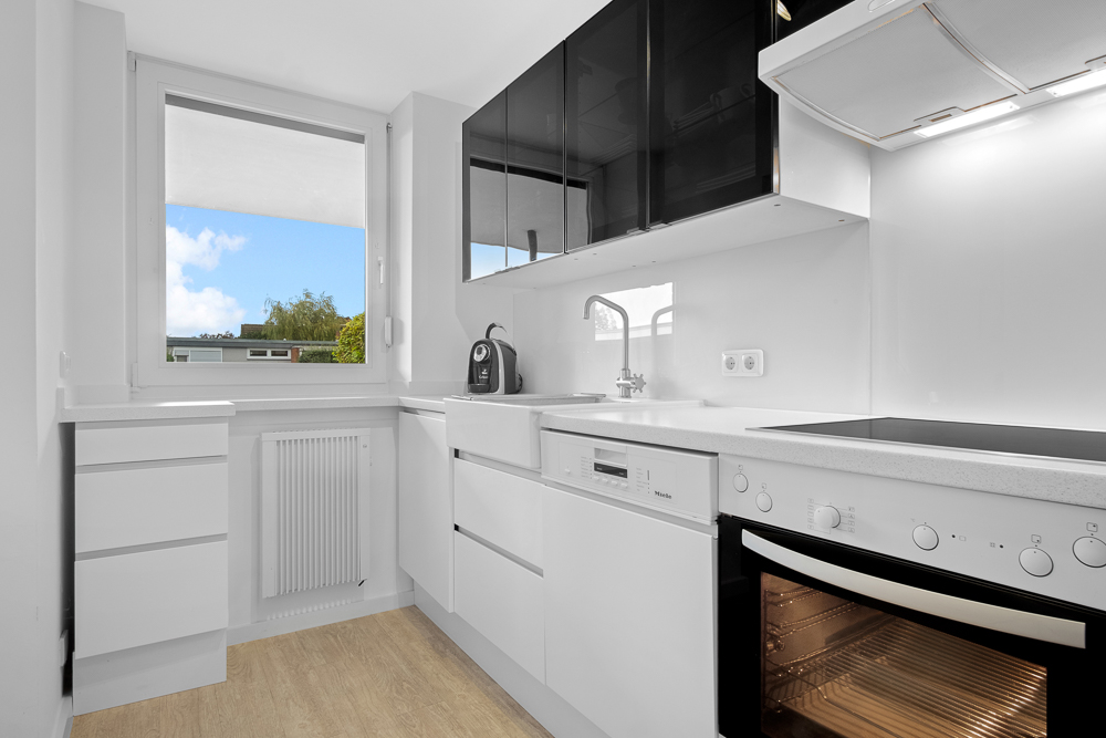 Moderne weiße Küche mit Herd, Ofen, Spüle, Geschirrspüler und Fenster mit Blick ins Freie.