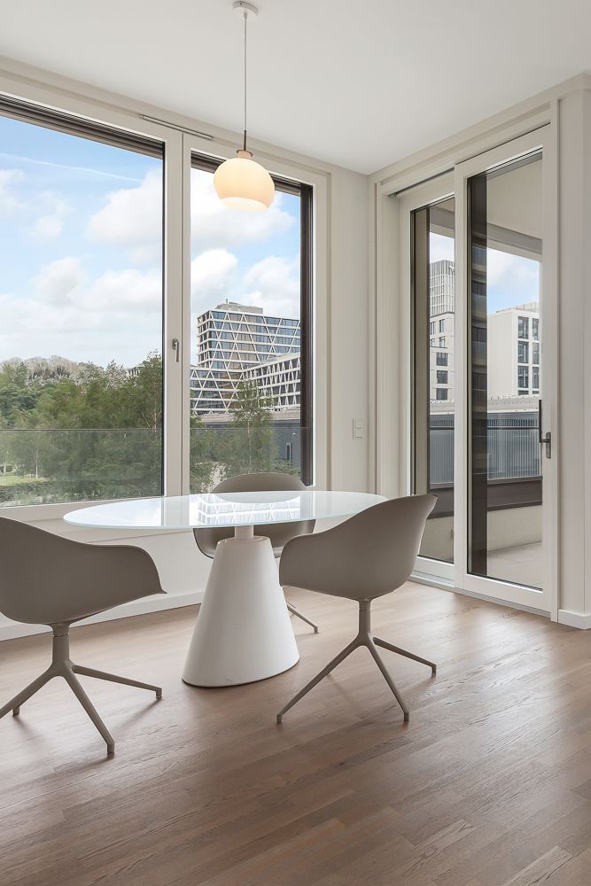 Heller Essbereich mit rundem Tisch, zwei Stühlen, Holzfußboden und großen Fenstern mit Stadtblick.