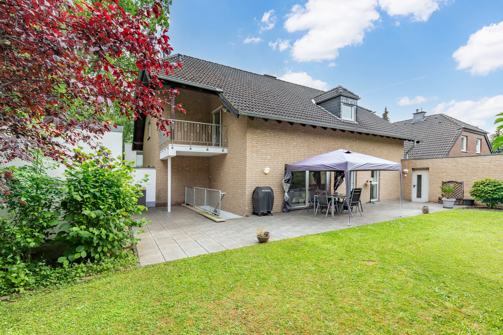 Garten mit Rasenfläche, Terrasse, Sitzgruppe mit Pavillon und modernem Haus im Hintergrund.