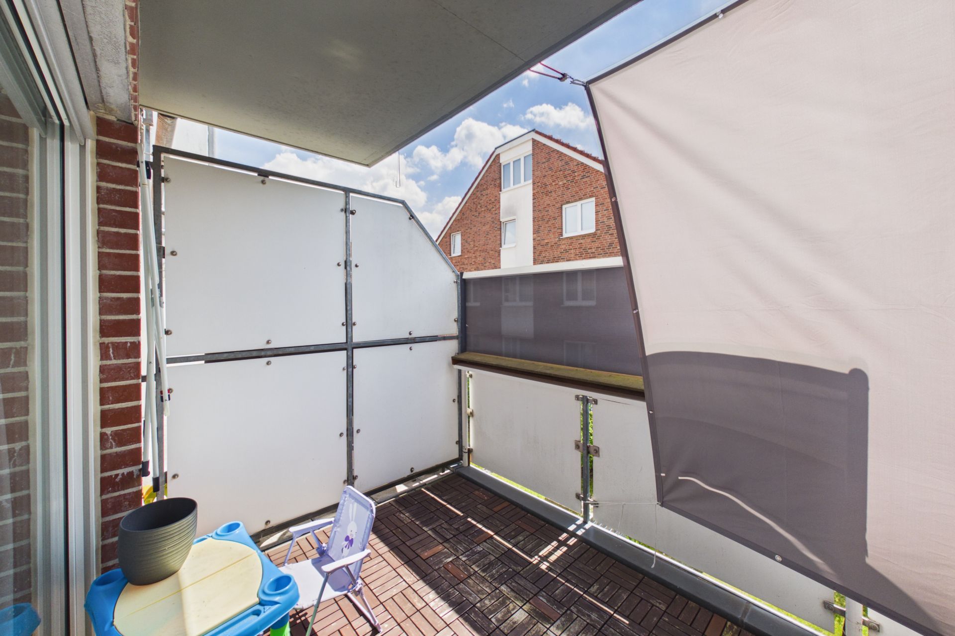 Kleiner Balkon mit Sichtschutz, Stuhl und Tisch, Blick auf Nachbargebäude.