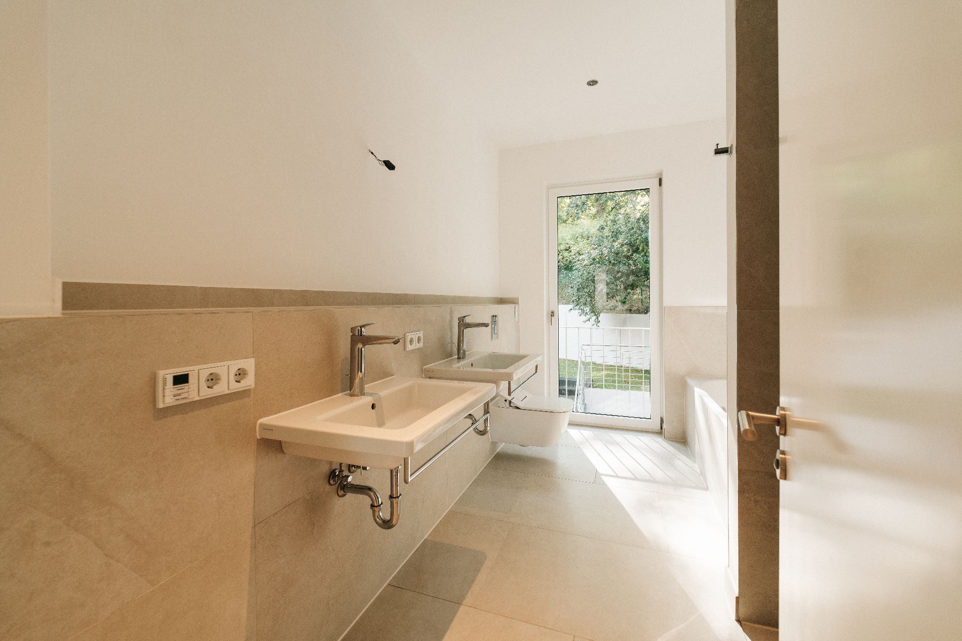 Modernes Badezimmer mit zwei Waschbecken, WC und Glastür mit Blick ins Grüne.