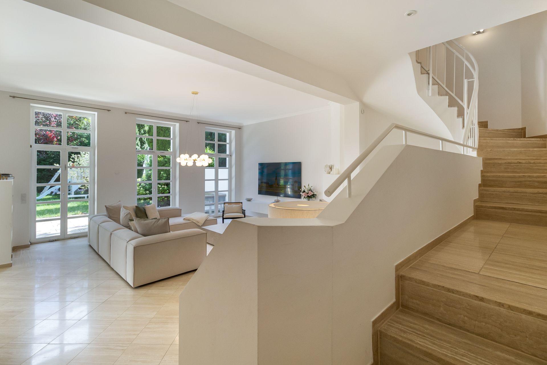 Helles Wohnzimmer mit Sofas, großem Fenster und Treppe mit Holzstufen im Vordergrund.