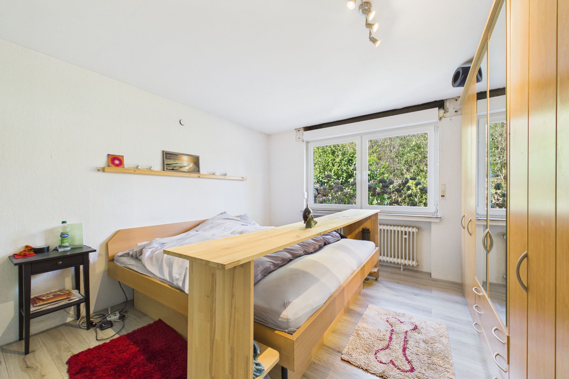 Helles Schlafzimmer mit Bett, Kleiderschrank, Nachttisch und großem Fenster mit Blick ins Grüne.