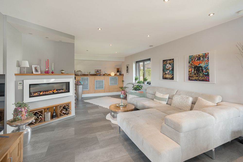 Modernes Wohnzimmer mit Kamin, großem Ecksofa und Wandbildern, angrenzender offener Küche.