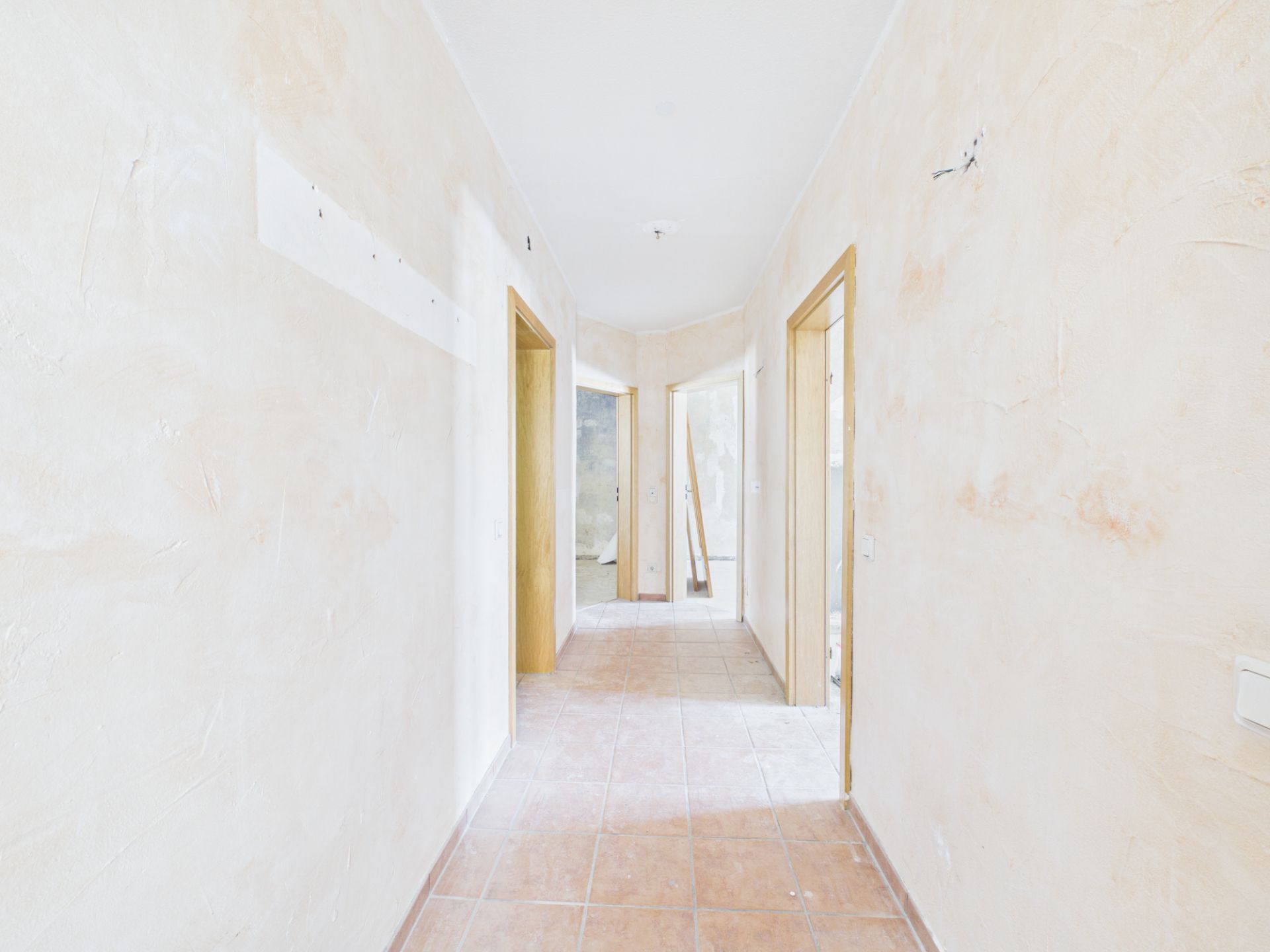 Heller Flur mit Fliesenboden und mehreren offenen Türen in einer Wohnung.