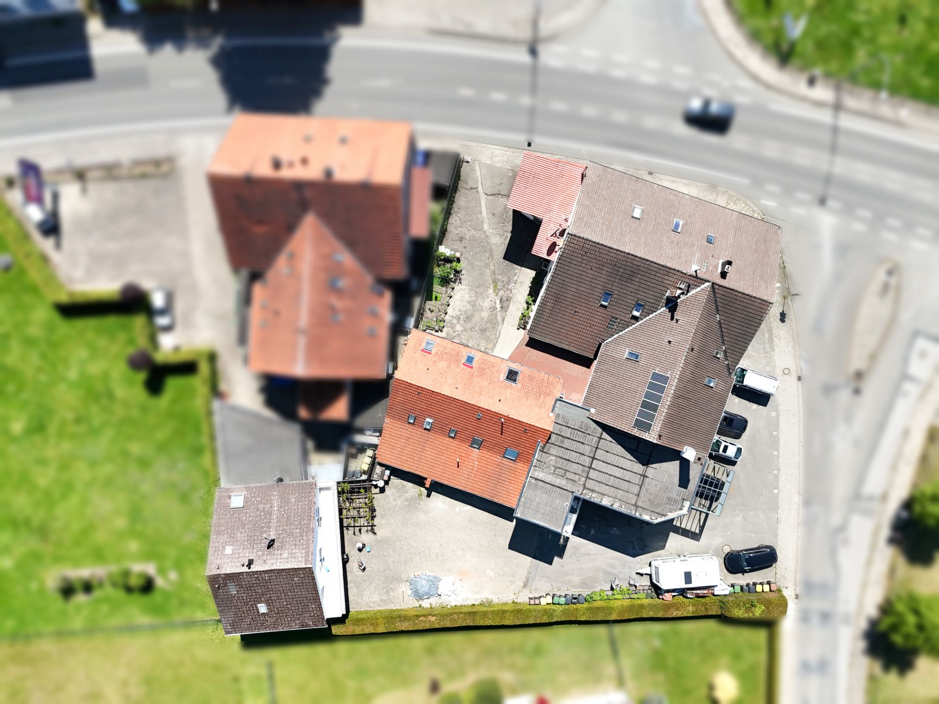 Luftaufnahme mehrerer Wohnhäuser mit Höfen und angrenzender Straße.