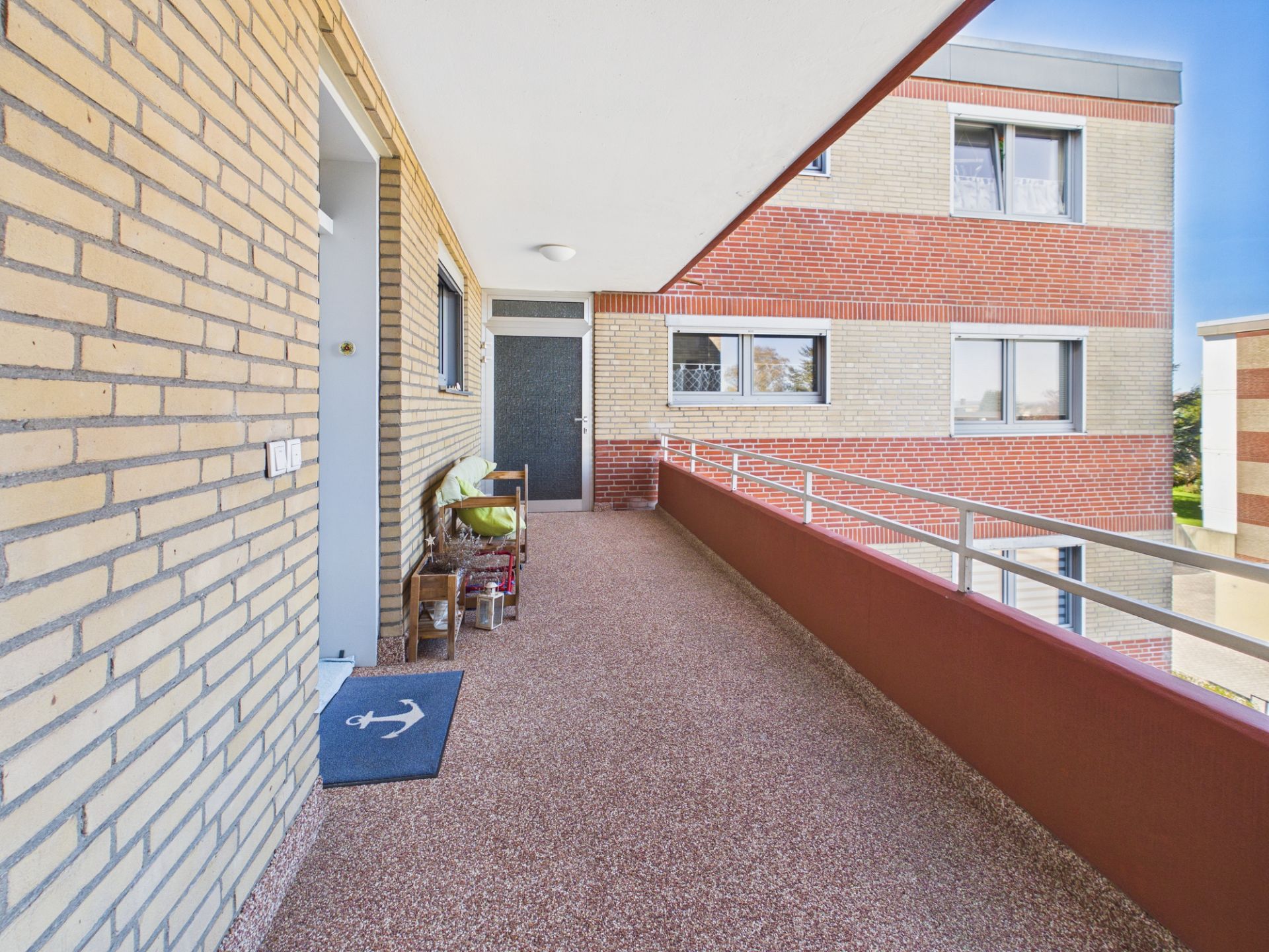 Langer offener Balkon mit Stühlen, Geländer und Blick auf gegenüberliegende Wohnung.