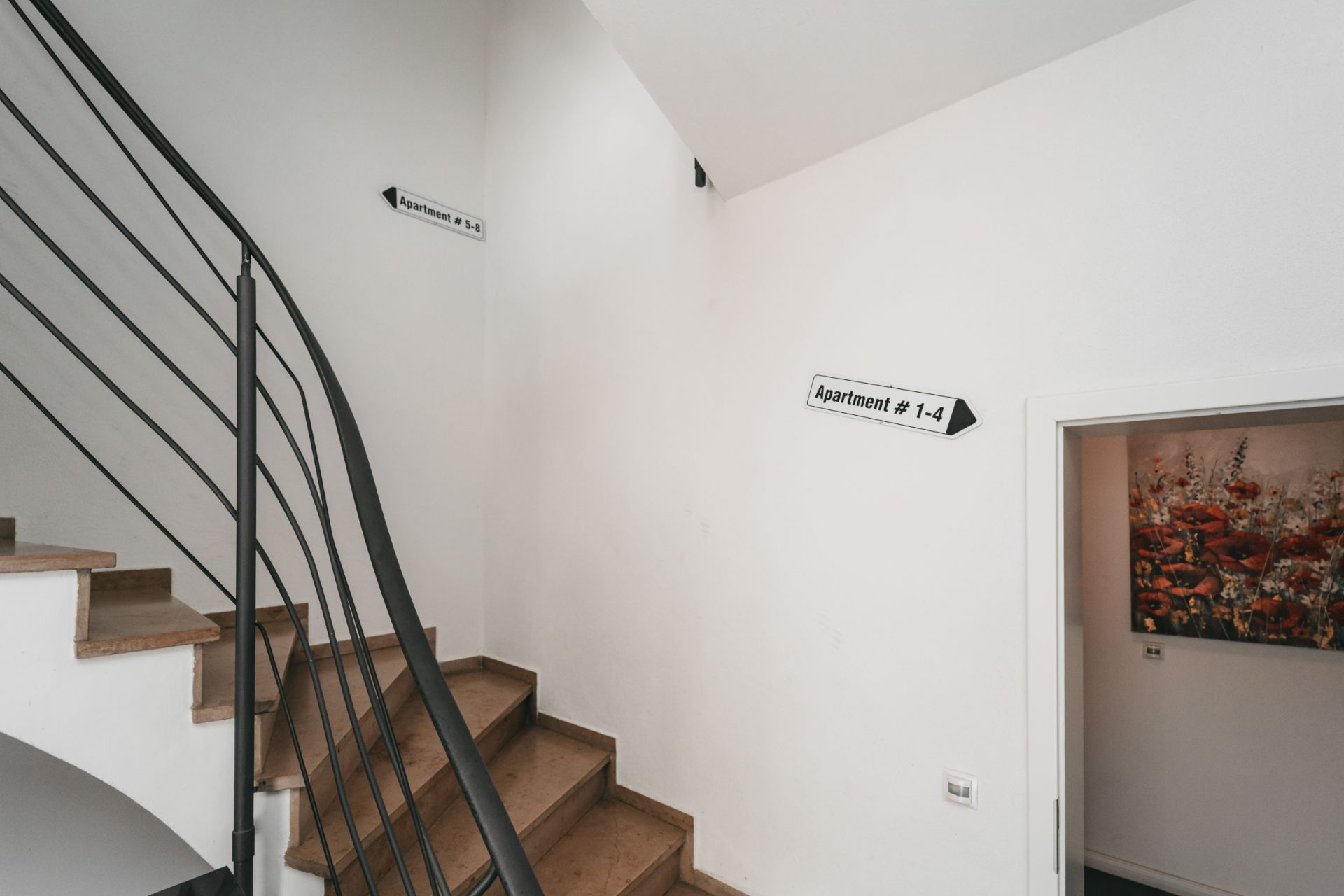 Treppenhaus mit Holzstufen, weißen Wänden und Richtungsschildern zu Apartments.