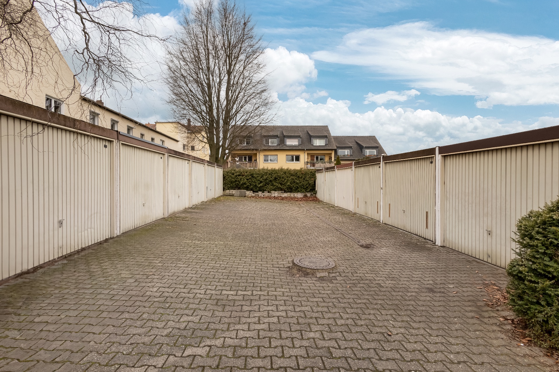Gepflasterter Hof mit Garagenreihen links und rechts, im Hintergrund Wohnhäuser und Bäume.