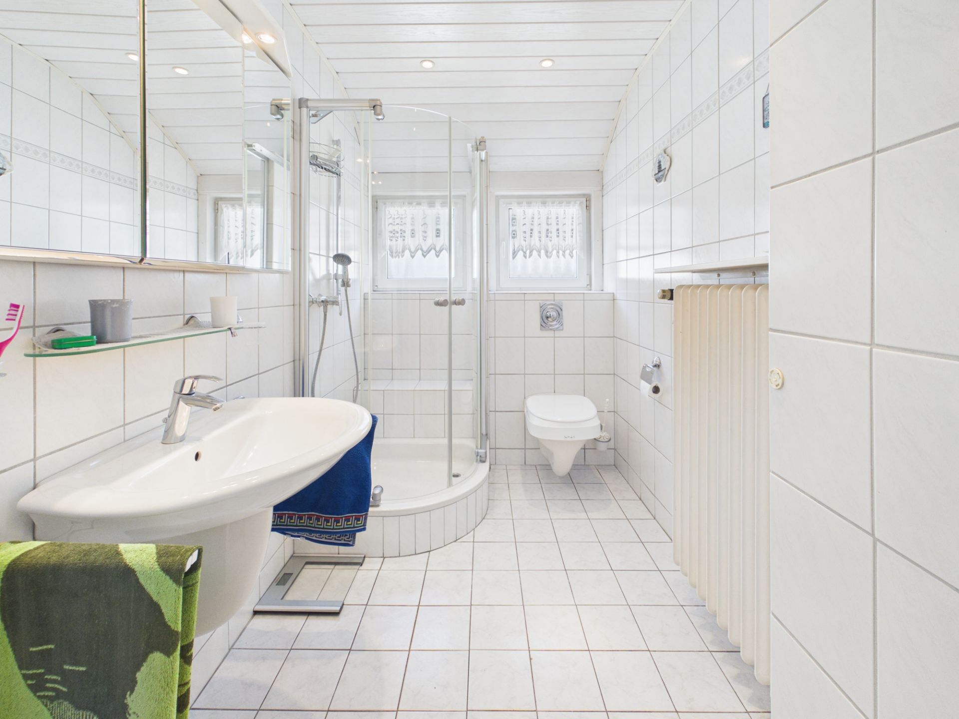 Helles Badezimmer mit Dusche, Waschbecken, WC und Handtuchheizkörper.