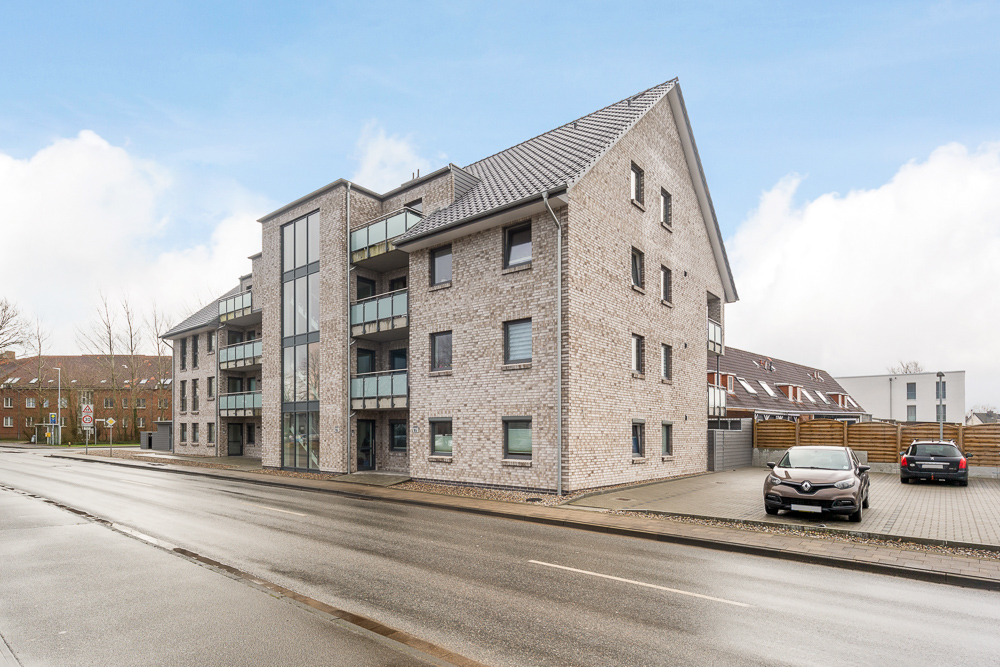 Modernes Mehrfamilienhaus mit Balkonen und Parkplätzen an einer Straße.