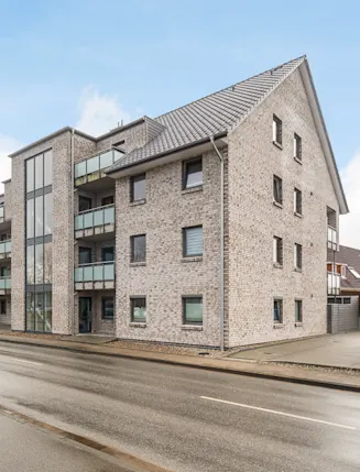 Modernes Mehrfamilienhaus mit Balkonen und Parkplätzen an einer Straße.