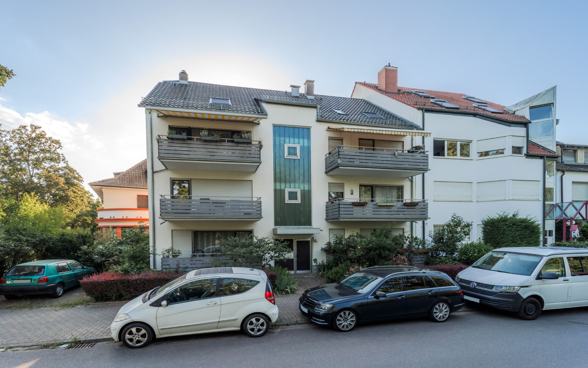 Dreistöckiges Wohnhaus mit Balkonen und parkenden Autos davor.