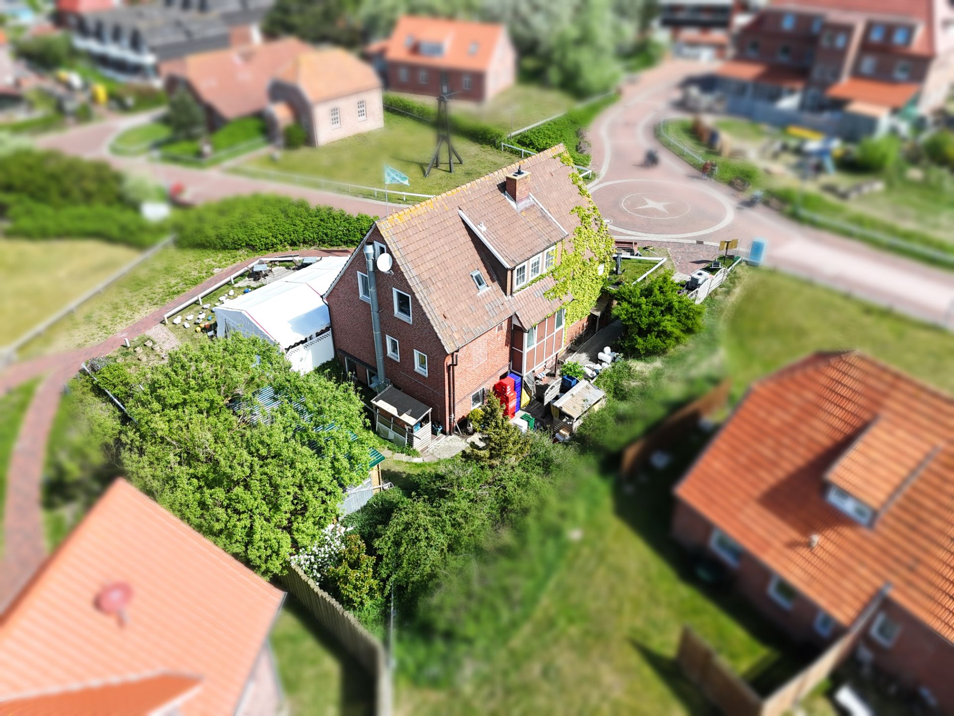 Backsteinwohnhaus mit Satteldach und Garten, umgeben von Wegen und weiteren Häusern.