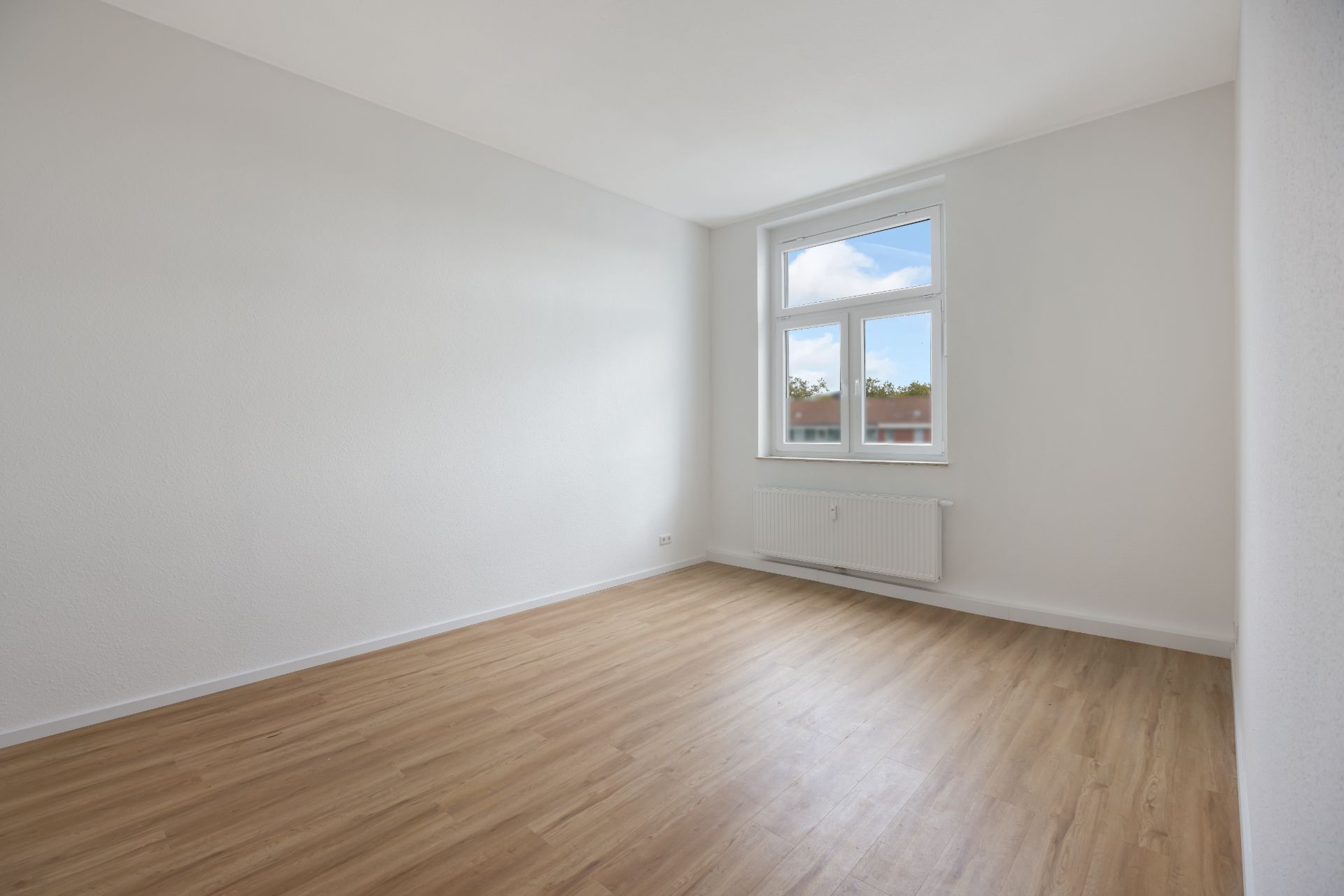 Heller, leerer Raum mit weißer Wand, Holzboden und einem Fenster.