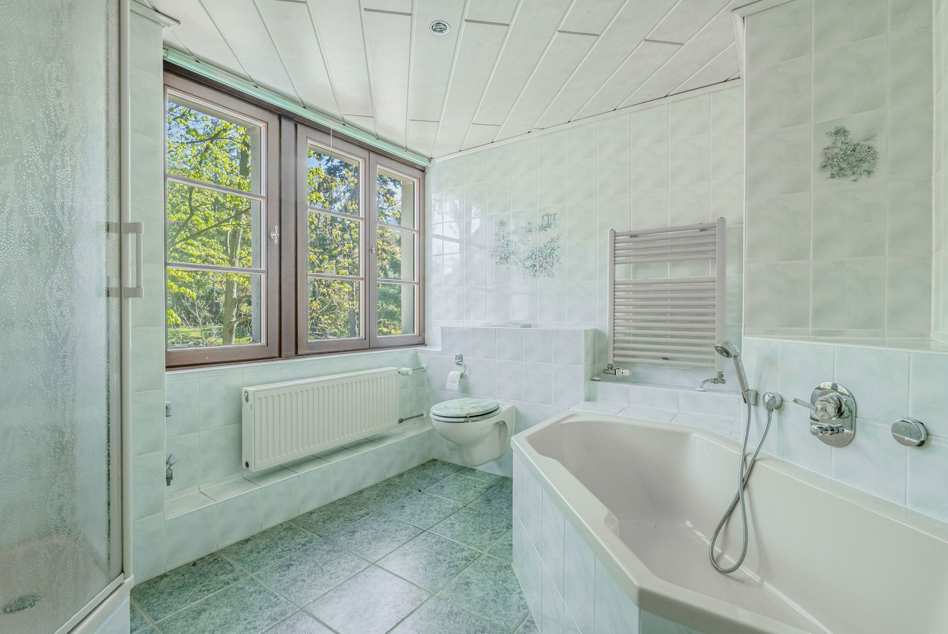 Helles Badezimmer mit Badewanne, Dusche, Toilette und großem Fenster.