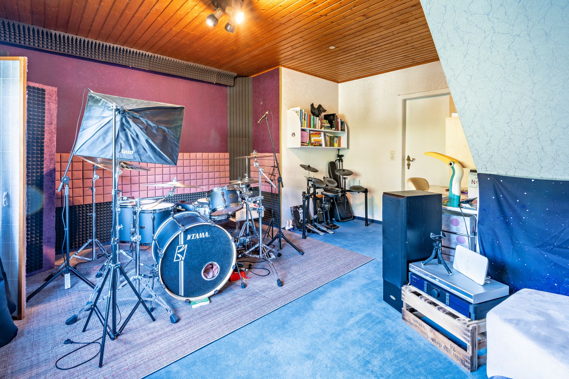 Musikraum mit Schlagzeug, elektronischem Schlagzeug und Regalen an der Wand.