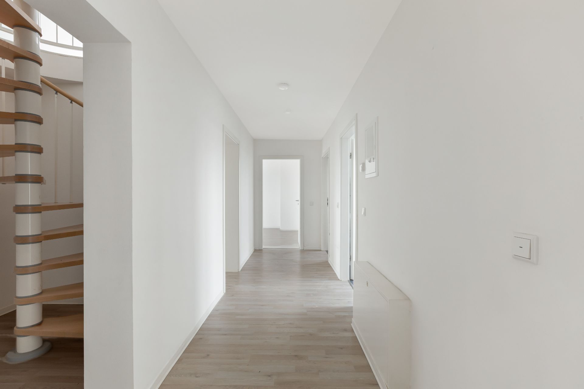 Heller Flur mit Holzboden, Türen zu mehreren Zimmern und einer Wendeltreppe links.
