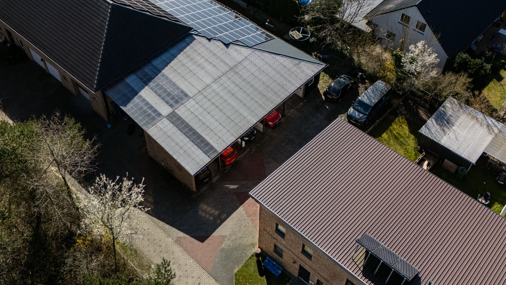 Luftaufnahme von Wohnhäusern, Carport mit Solarpanelen und geparkten Autos im Hof.