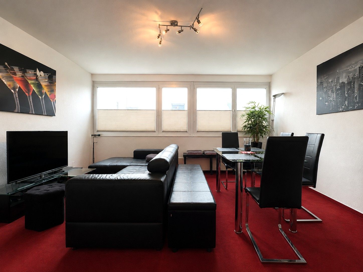 Modernes Wohnzimmer mit schwarzem Sofa, Esstisch, Fernseher und großem Fenster, roter Teppichboden.