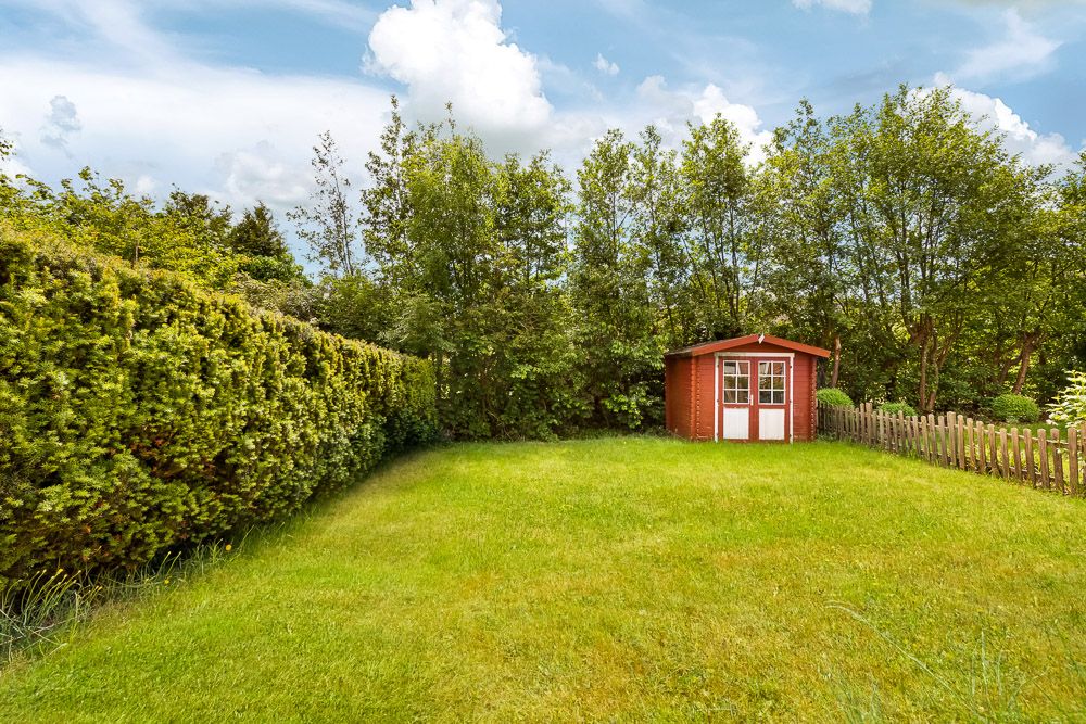 Grüner Garten mit Rasenfläche, Hecke und einem kleinen roten Gartenhaus aus Holz.
