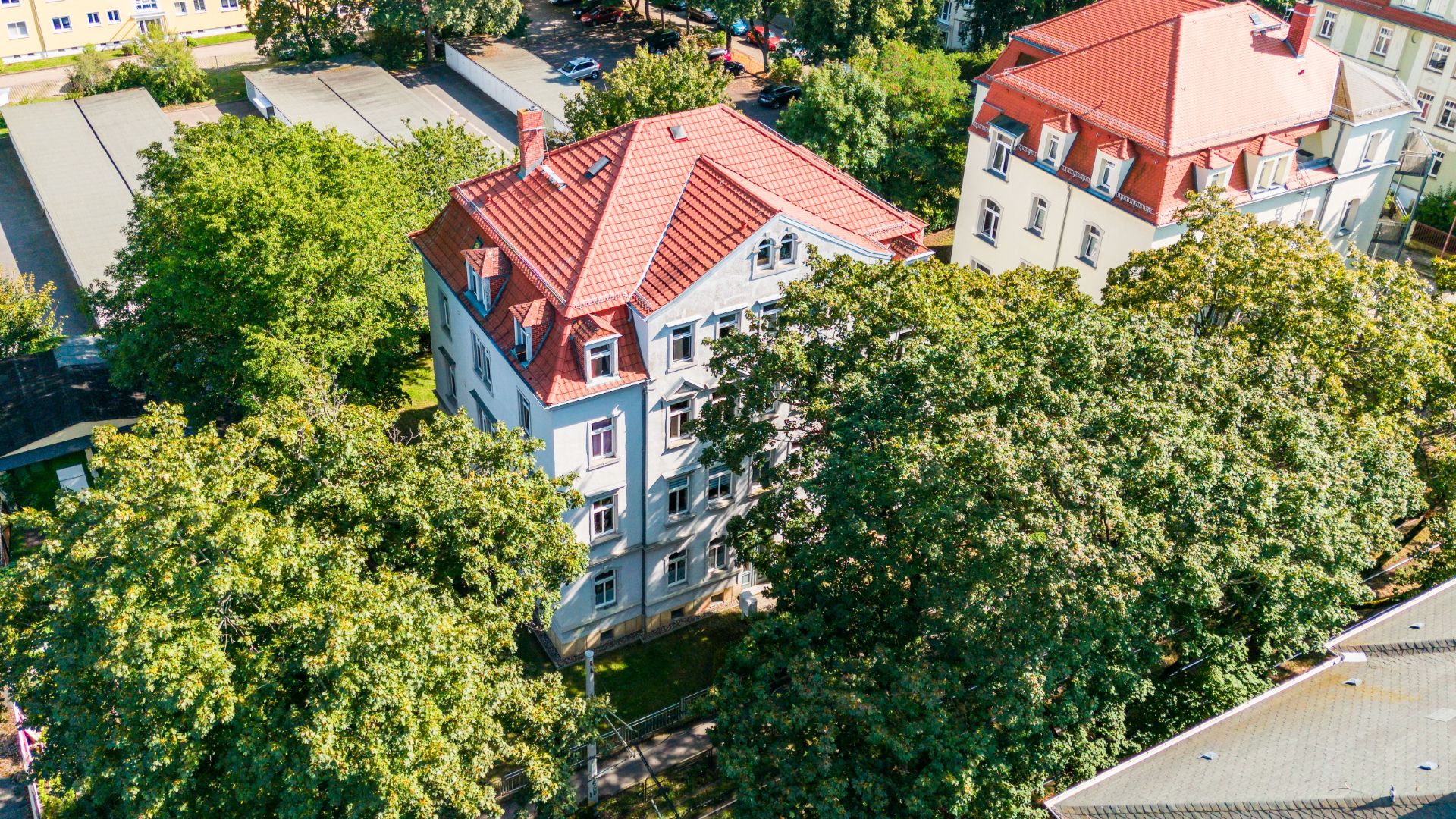 Mehrstöckiges Wohnhaus mit rotem Dach, umgeben von Bäumen, aus der Vogelperspektive.