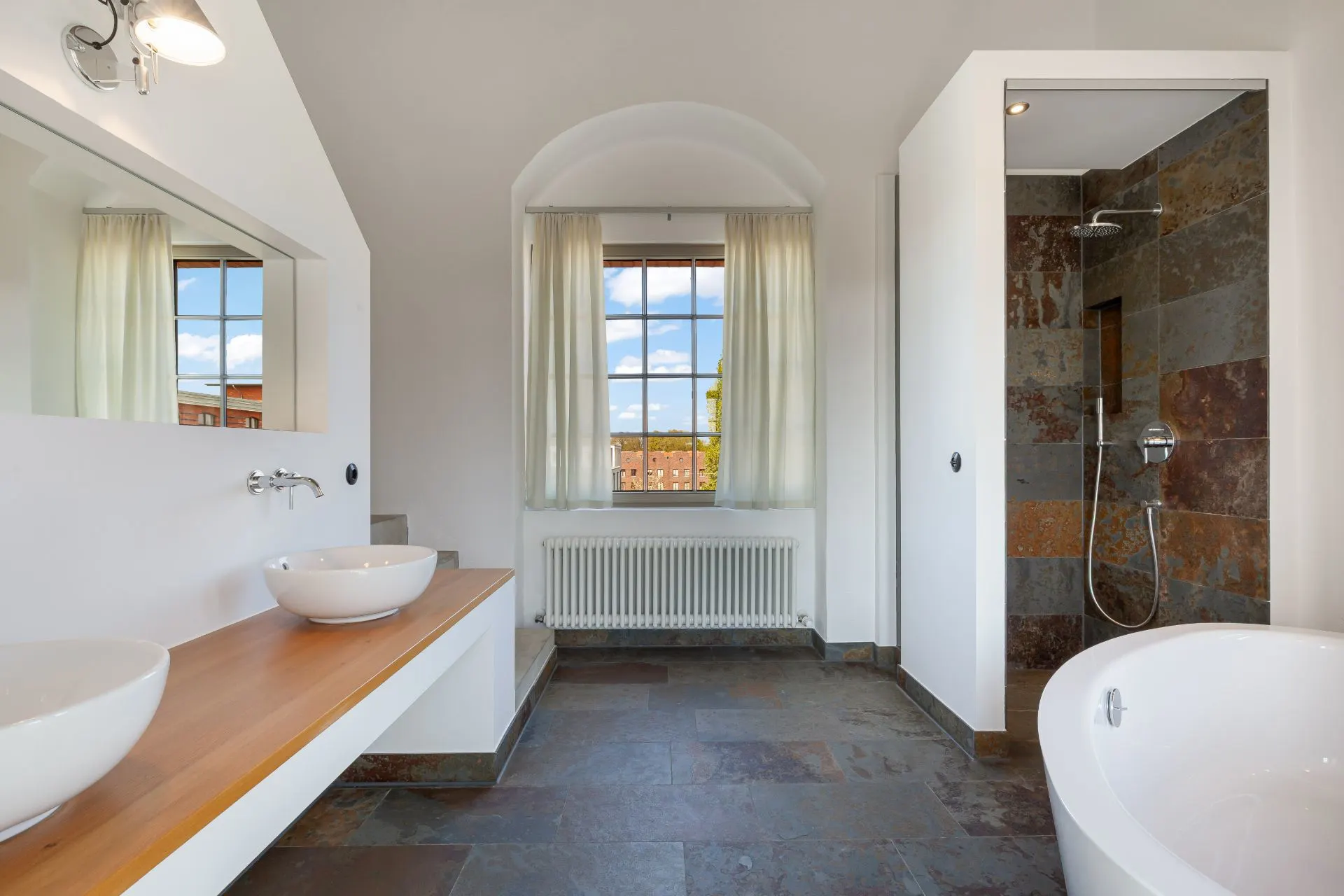 Modernes Badezimmer mit zwei Waschbecken, Dusche, Badewanne und großem Fenster mit Vorhängen.