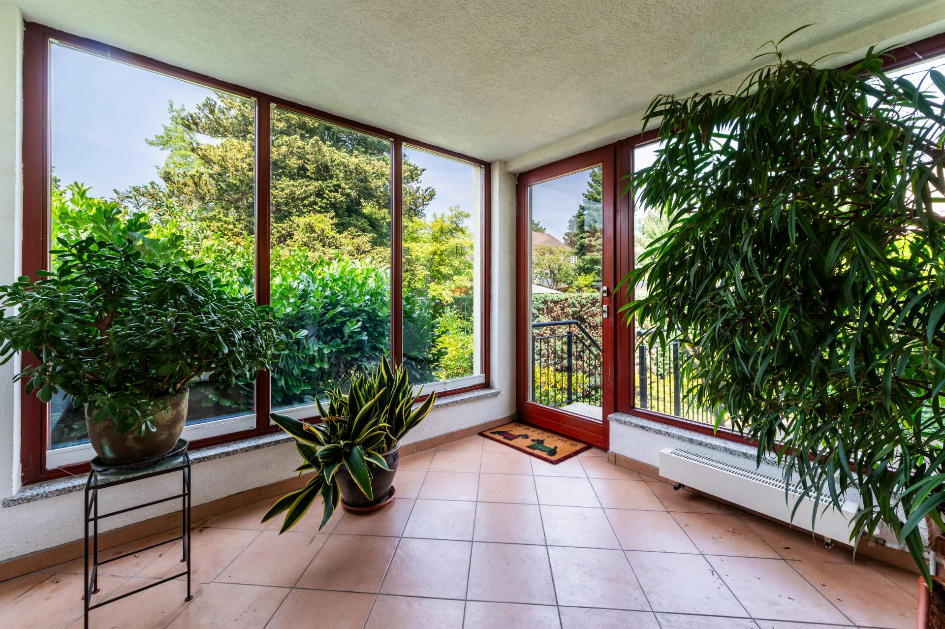 Heller Wintergarten mit großen Fenstern, Fliesenboden und mehreren grünen Zimmerpflanzen.