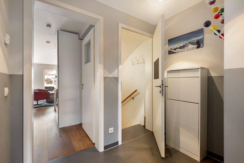 Flur mit drei Türen, grauem Boden, modernem Schuhschrank und Wandbild.