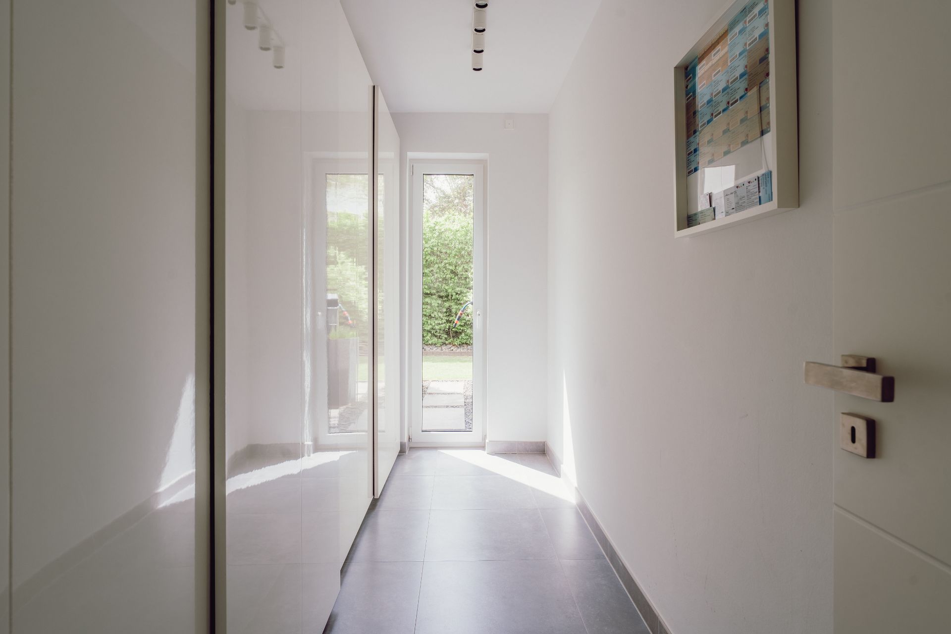 Heller Flur mit großen Einbauschränken, Glastür am Ende und Bild an der Wand.
