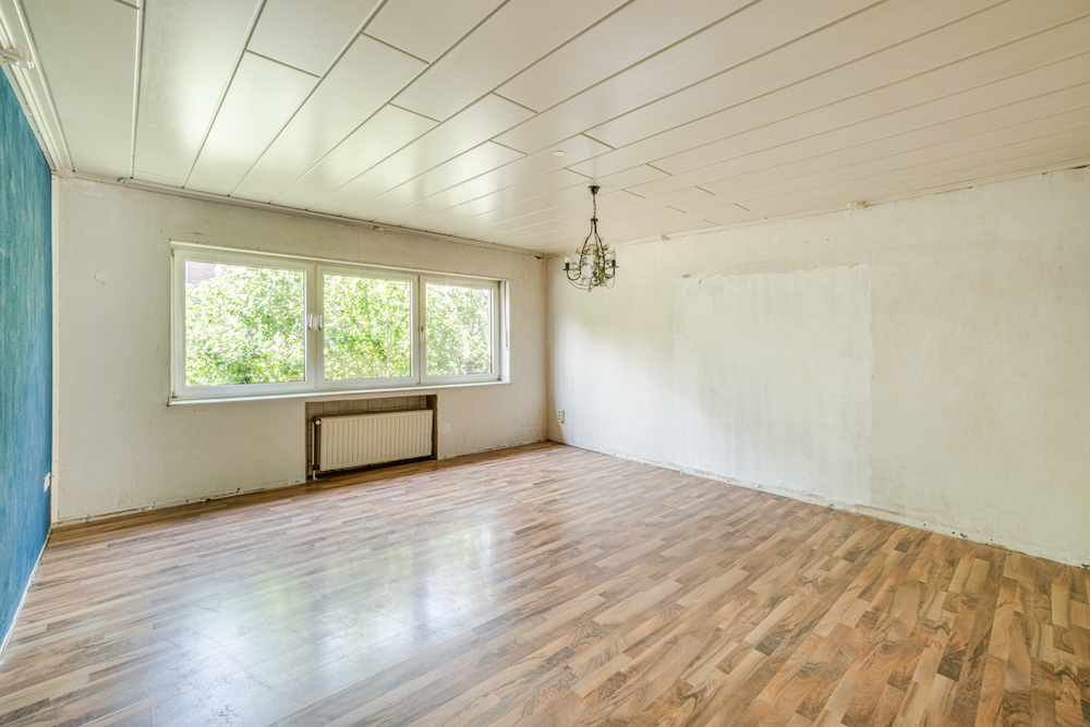 Leeres Zimmer mit Holzfußboden, großem Fenster, Heizung und Deckenleuchte.